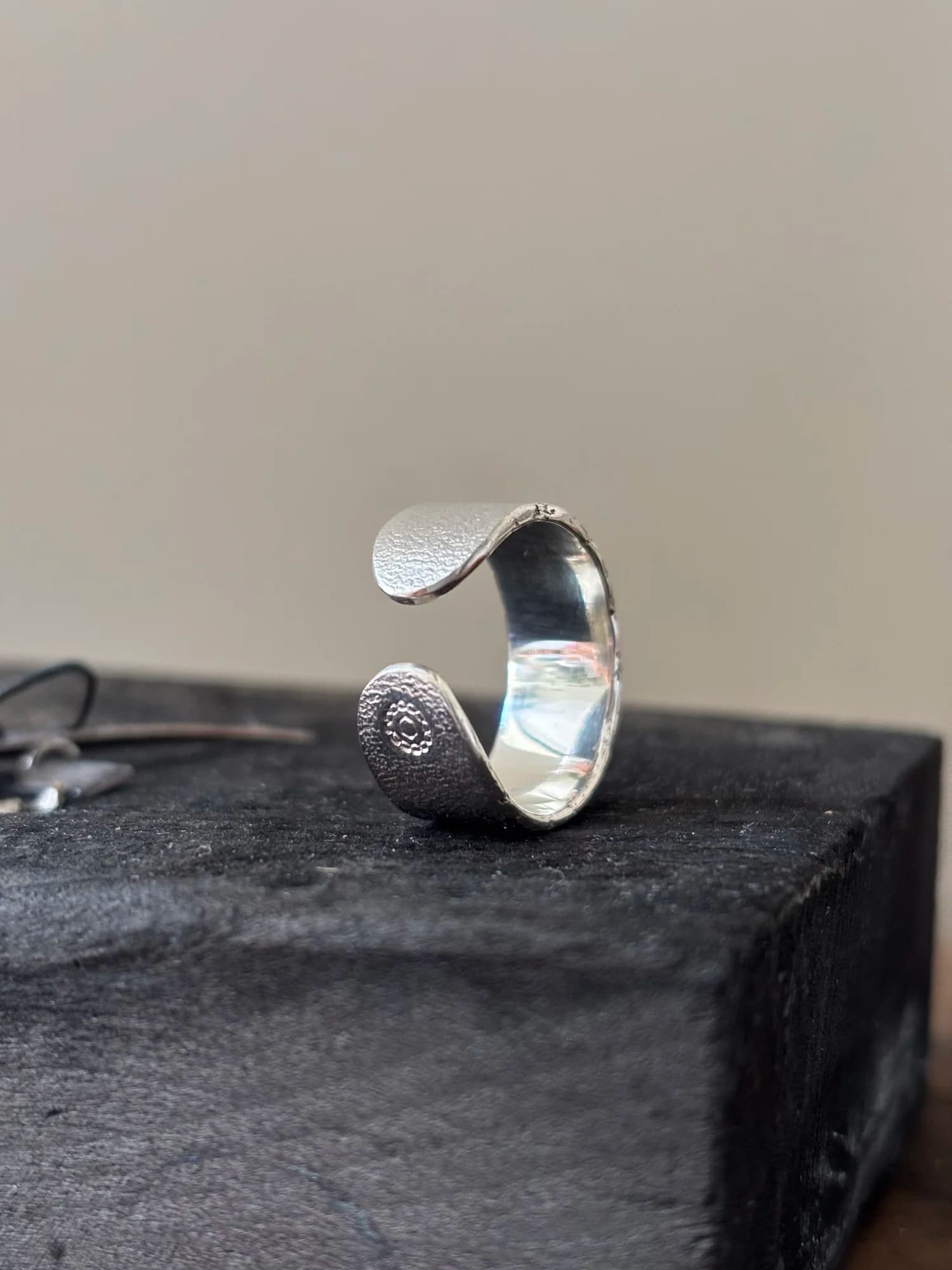 Offener Sterlingsilber-Ring mit körnig gewalzter Oberfläche, aufrecht stehend; ein rundes Ende trägt die MADU JIWA-Punze, die Innenseite ist blank poliert.