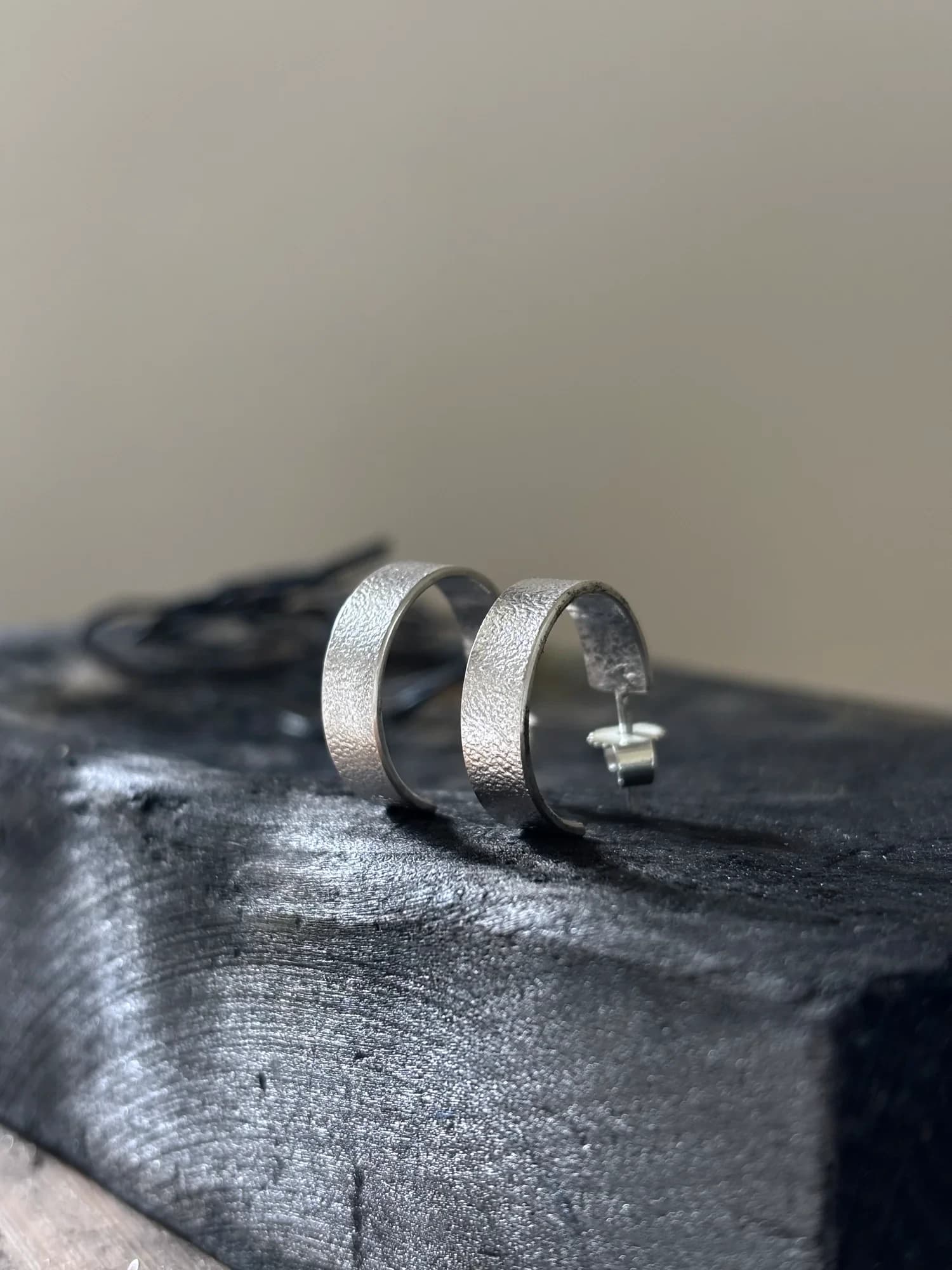 Zwei handgemachte Silber-Creolen mit feiner Walzentextur auf dunklem Werkstattblock.